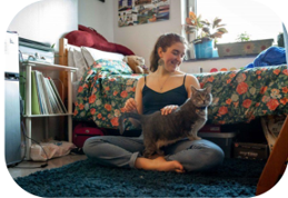 Woman sitting cross-legged on the floor holding a cat in her dorm room. 